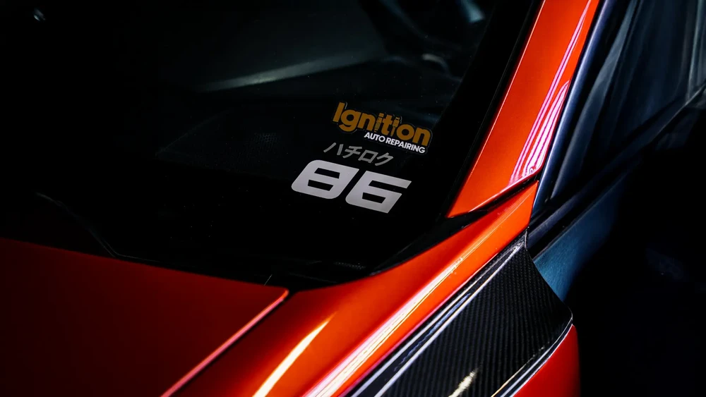 Intérieur d'un véhicule sportif avec vitrage teinté noir portant les inscriptions "Ignition AUTO REPAIRING" en lettrage doré et "86" en blanc