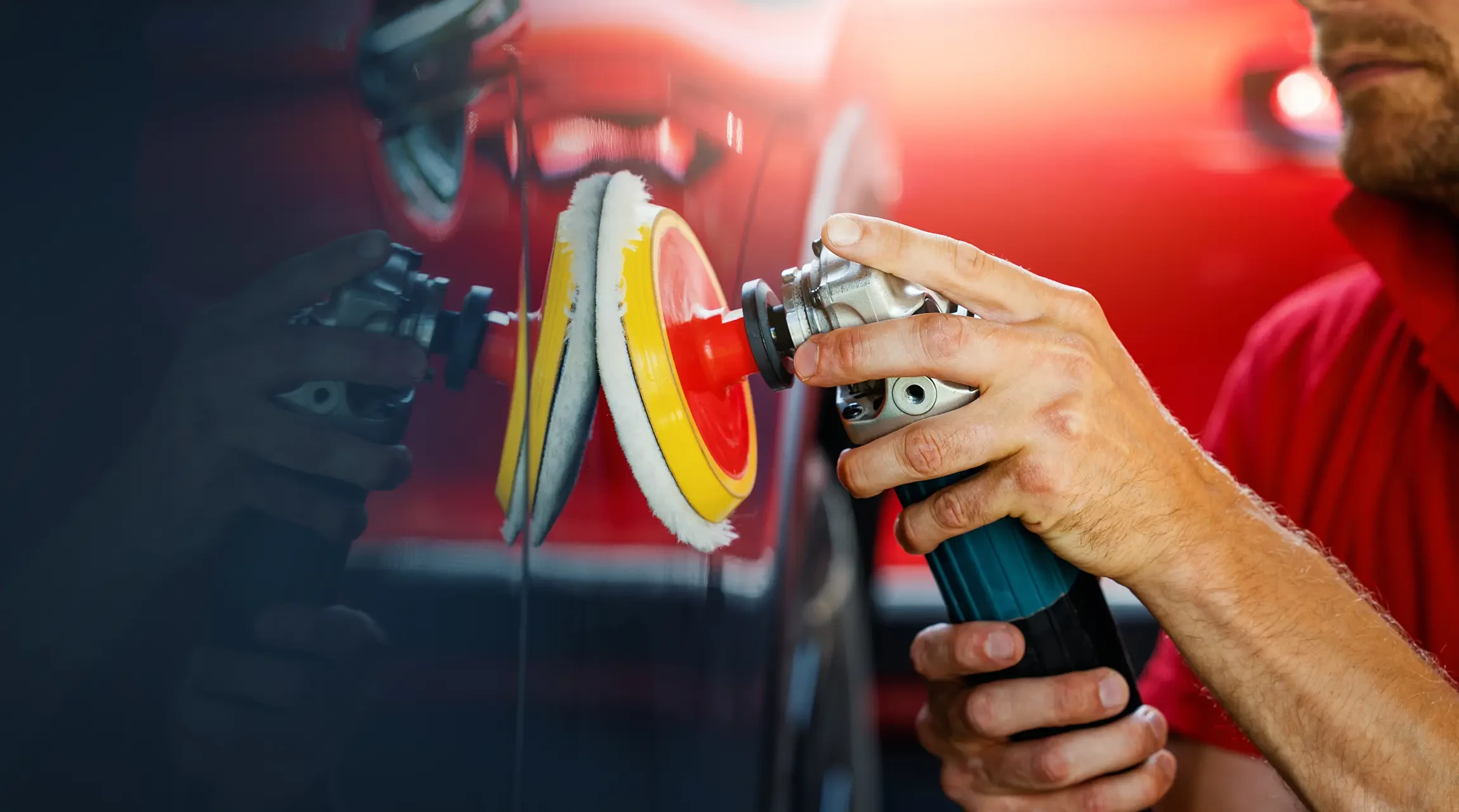 Homme effectuant le polissage d'une carrosserie automobile rouge dans un atelier